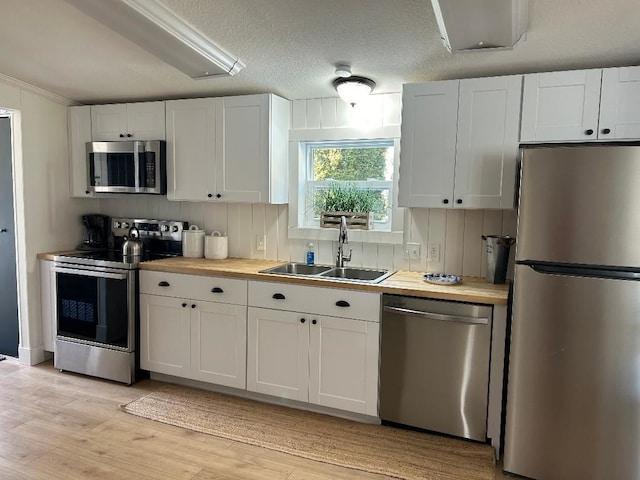 kitchen featuring light wood finished floors, white cabinets, appliances with stainless steel finishes, wooden counters, and a sink