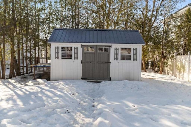 snow covered structure featuring an outbuilding, fence, and a shed