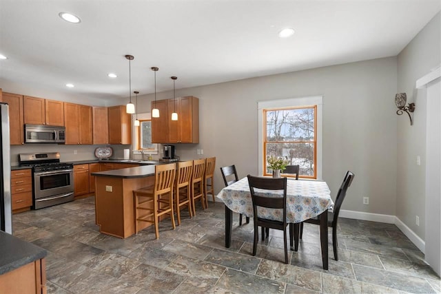 kitchen with brown cabinets, stainless steel appliances, dark countertops, baseboards, and a kitchen breakfast bar