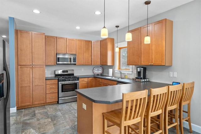 kitchen with a peninsula, dark countertops, appliances with stainless steel finishes, and a sink