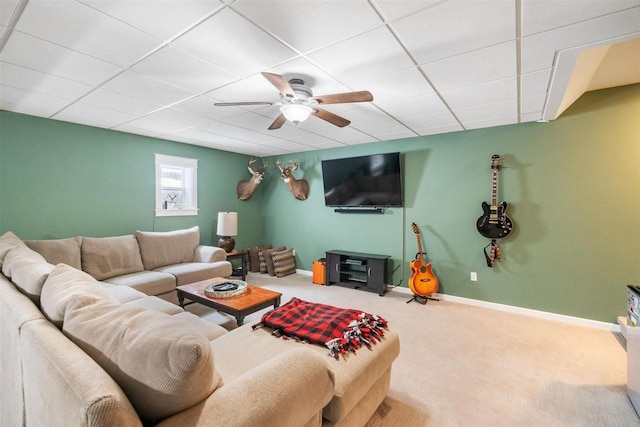 living room featuring ceiling fan, carpet floors, a drop ceiling, and baseboards