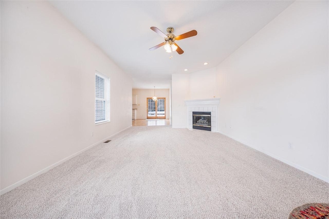 unfurnished living room with visible vents, a tiled fireplace, a ceiling fan, carpet flooring, and baseboards