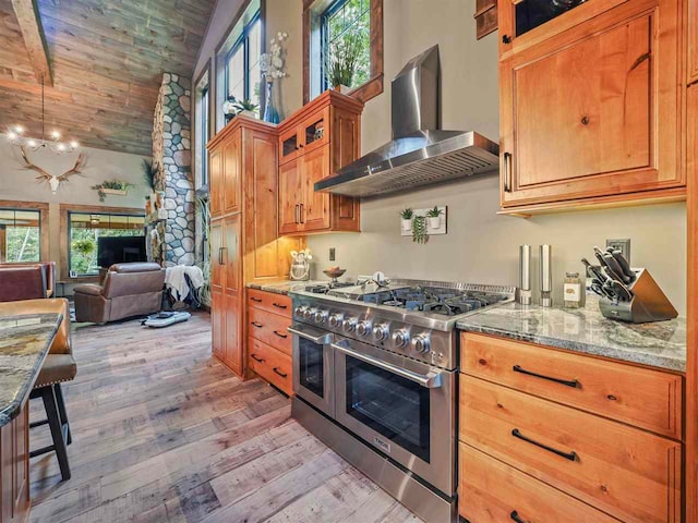 kitchen with range with two ovens, light stone counters, wooden ceiling, light wood-style floors, and wall chimney exhaust hood