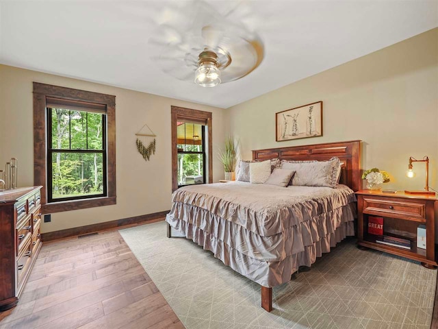 bedroom with light wood finished floors, ceiling fan, visible vents, and baseboards