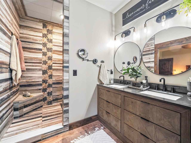 bathroom with double vanity, a walk in shower, a sink, and wood finished floors