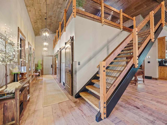 staircase with a notable chandelier, wood-type flooring, a high ceiling, a barn door, and wood ceiling