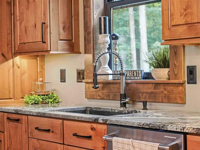 kitchen featuring stainless steel dishwasher, stone countertops, a sink, and brown cabinets