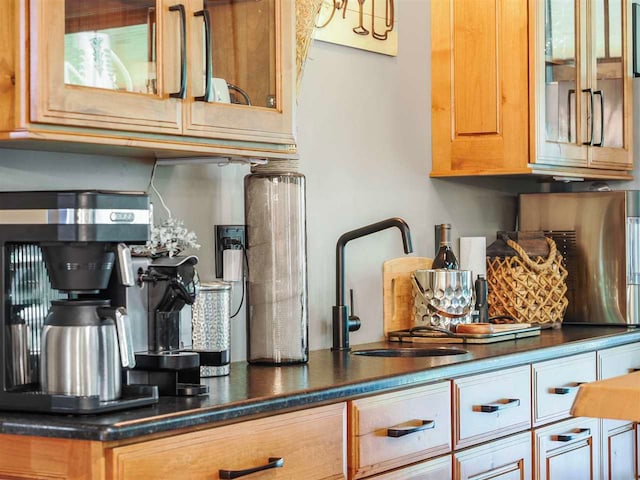 kitchen featuring dark countertops, a sink, glass insert cabinets, and brown cabinets