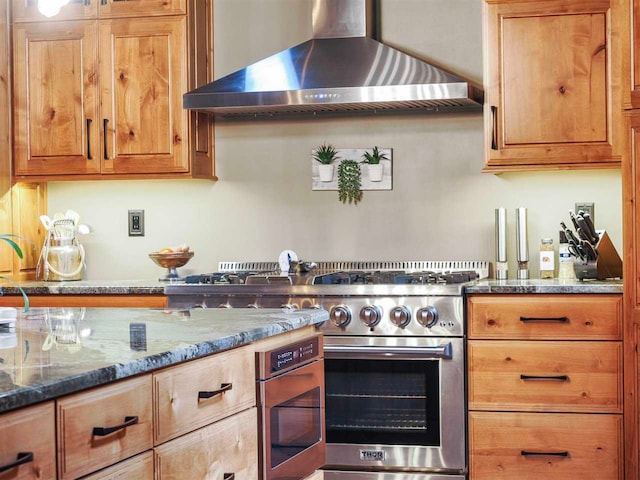 kitchen with dark stone countertops, wall chimney exhaust hood, and high end stainless steel range