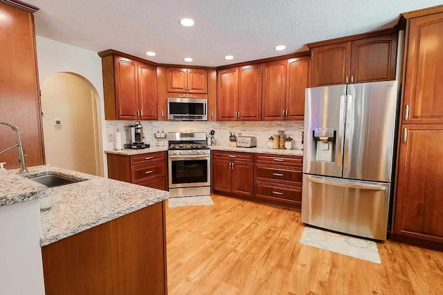 kitchen with arched walkways, stainless steel appliances, a sink, light stone countertops, and light wood-type flooring