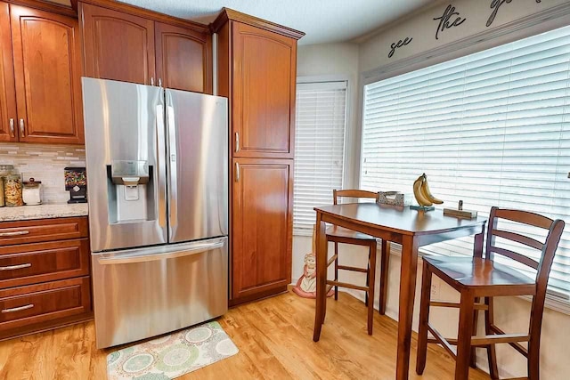 kitchen with light stone counters, tasteful backsplash, light wood-style flooring, brown cabinetry, and stainless steel fridge