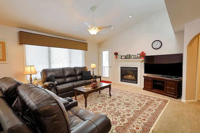 carpeted living area with arched walkways, a ceiling fan, baseboards, vaulted ceiling, and a glass covered fireplace