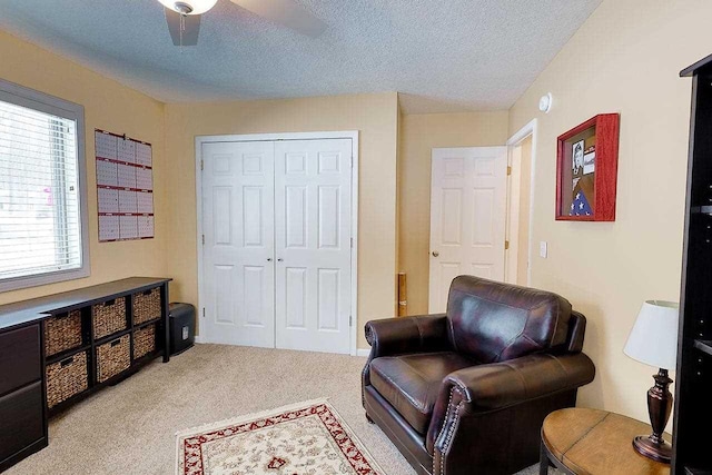 living area with a ceiling fan, light colored carpet, and a textured ceiling