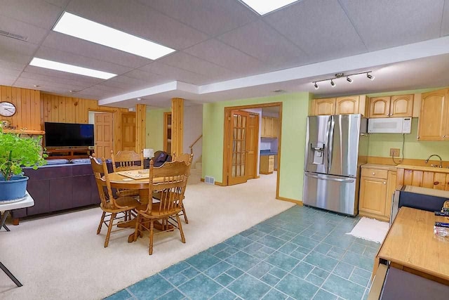 carpeted dining space with visible vents, wood walls, and a drop ceiling