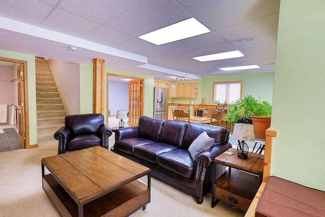 living area with stairway, a drop ceiling, and light colored carpet