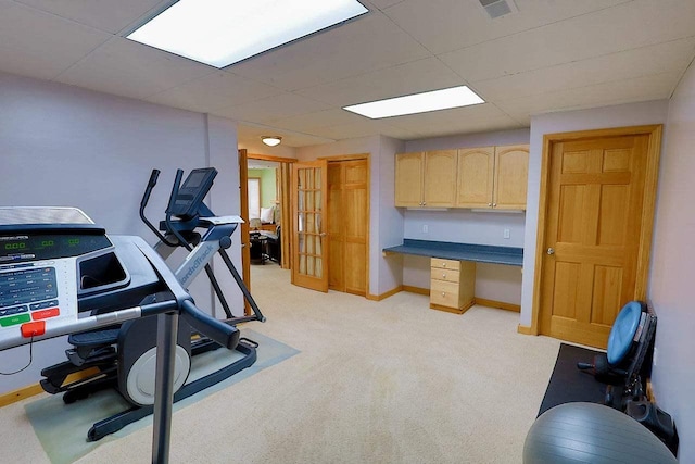 workout area featuring baseboards, built in desk, a paneled ceiling, and light colored carpet