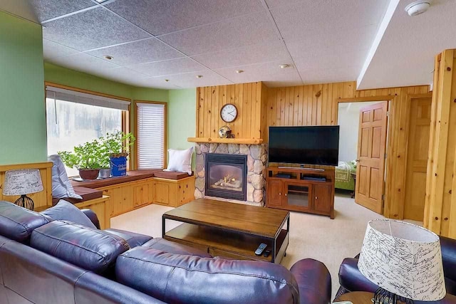 living room with light carpet, a stone fireplace, and wood walls