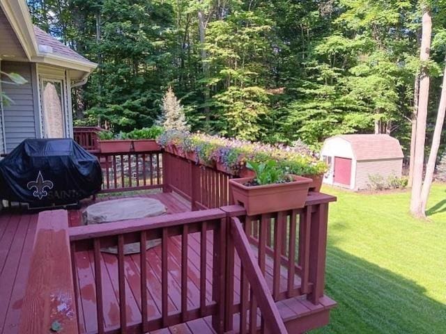 wooden terrace featuring an outbuilding, a grill, a lawn, and a storage unit