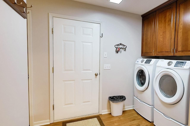 laundry area with cabinet space, baseboards, washer and clothes dryer, and light wood finished floors