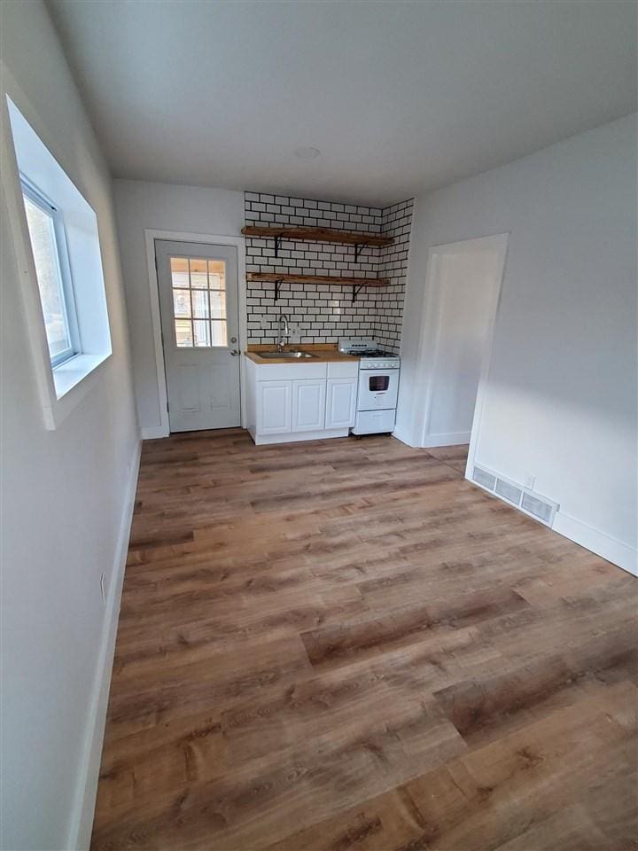 bar featuring white gas stove, visible vents, decorative backsplash, light wood-type flooring, and baseboards