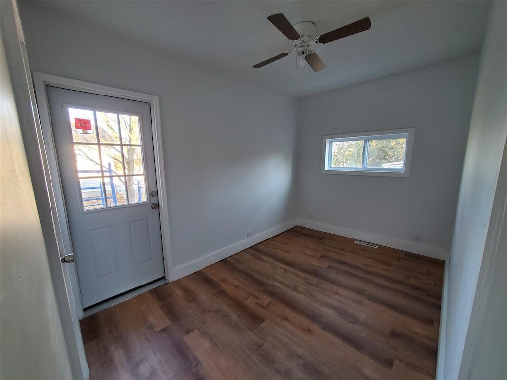 doorway featuring a ceiling fan, visible vents, baseboards, and wood finished floors