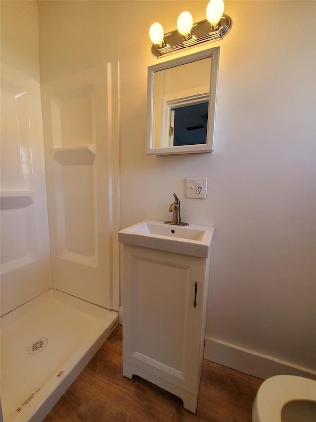 bathroom featuring toilet, wood finished floors, vanity, baseboards, and a stall shower