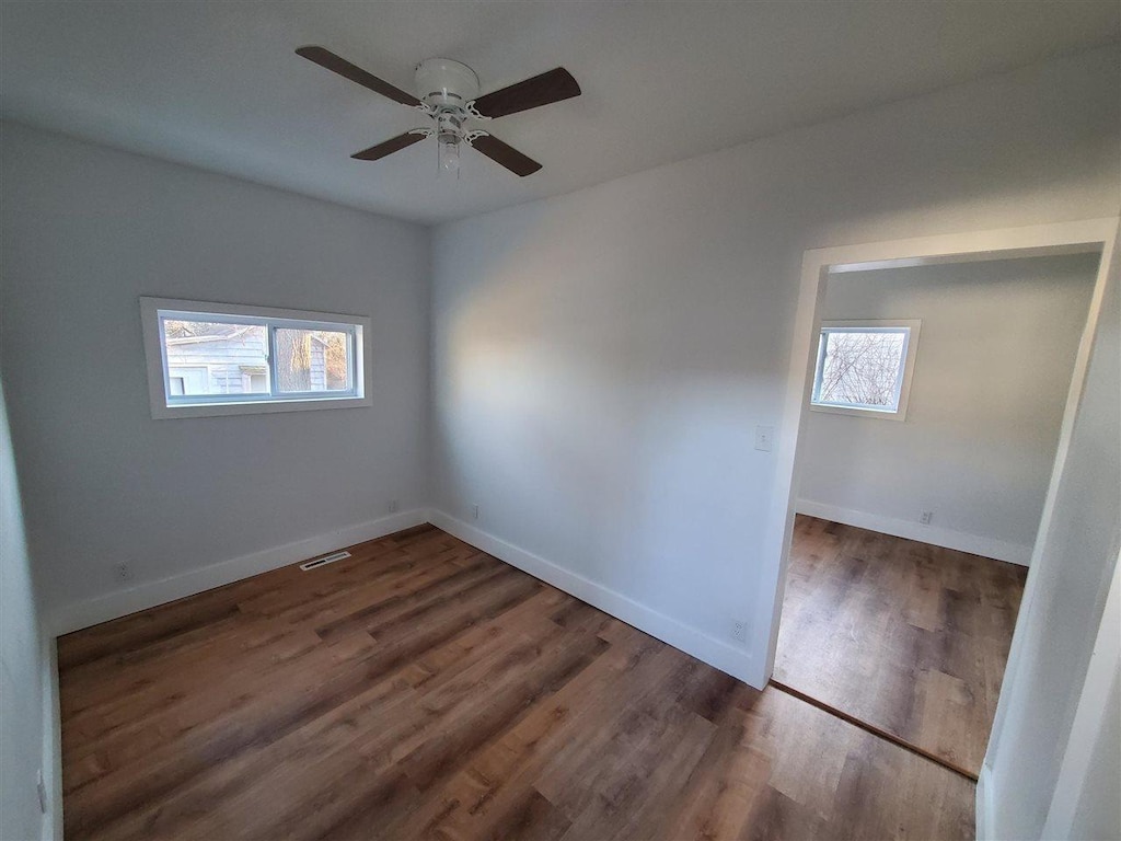 spare room with a ceiling fan, wood finished floors, visible vents, and baseboards