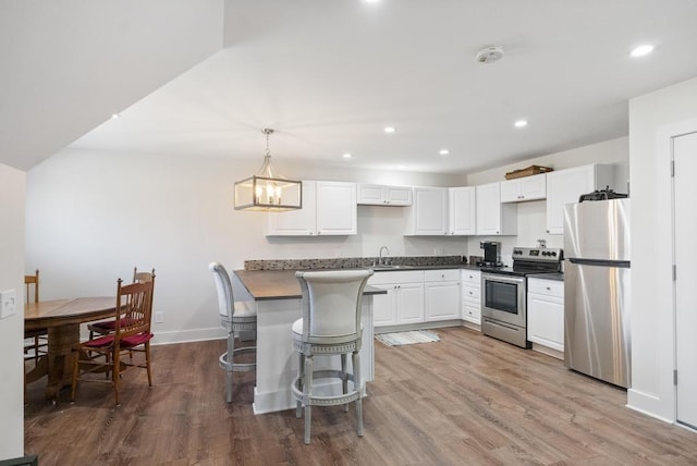 kitchen with dark countertops, wood finished floors, recessed lighting, stainless steel appliances, and white cabinets