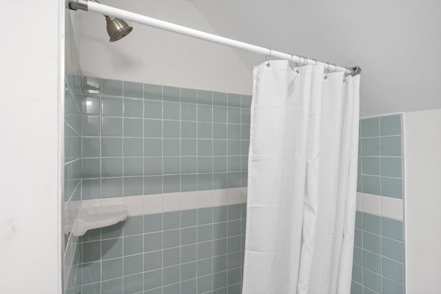 full bathroom featuring a tile shower and vaulted ceiling