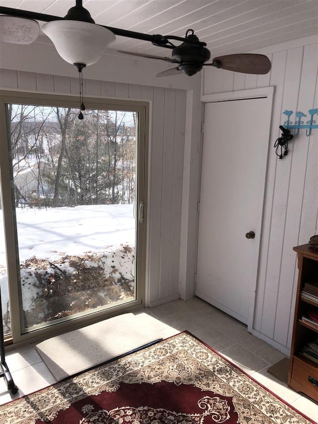 entryway featuring light tile patterned flooring, wood walls, and a ceiling fan