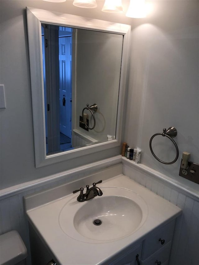 half bath with toilet, wainscoting, and vanity