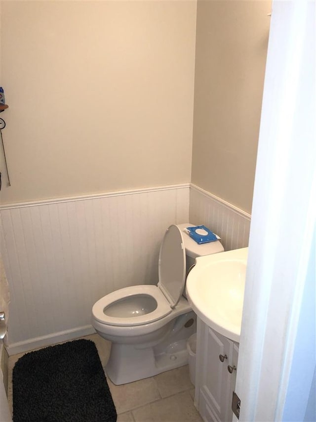 half bathroom with a wainscoted wall, toilet, vanity, and tile patterned flooring