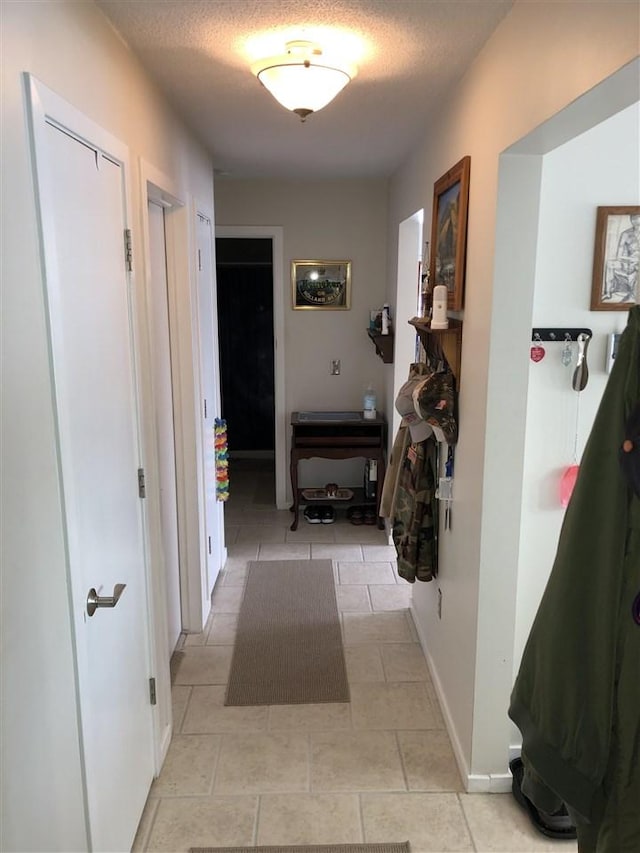 hall with light tile patterned floors, a textured ceiling, and baseboards