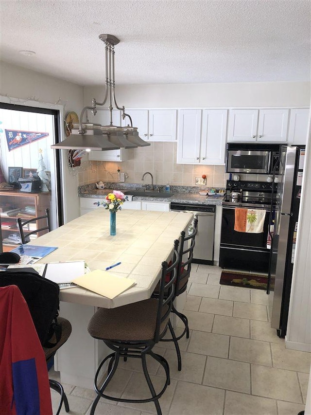 kitchen featuring tile countertops, stainless steel appliances, white cabinets, decorative light fixtures, and tasteful backsplash