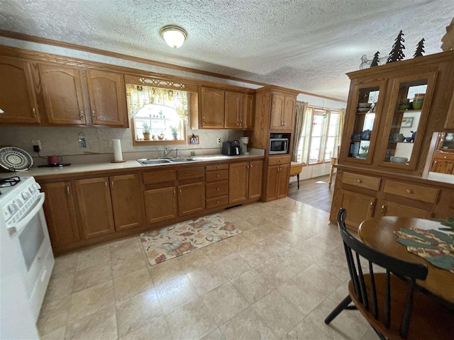 kitchen with a sink, light countertops, white range oven, crown molding, and brown cabinets