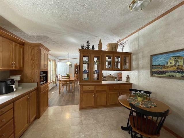 kitchen featuring brown cabinetry, stainless steel microwave, crown molding, and light countertops