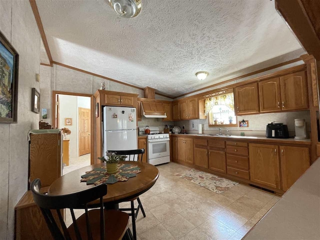 kitchen with brown cabinets, white appliances, crown molding, and lofted ceiling