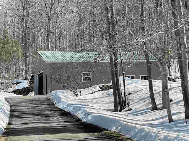 view of snow covered exterior featuring stucco siding, metal roof, and a garage