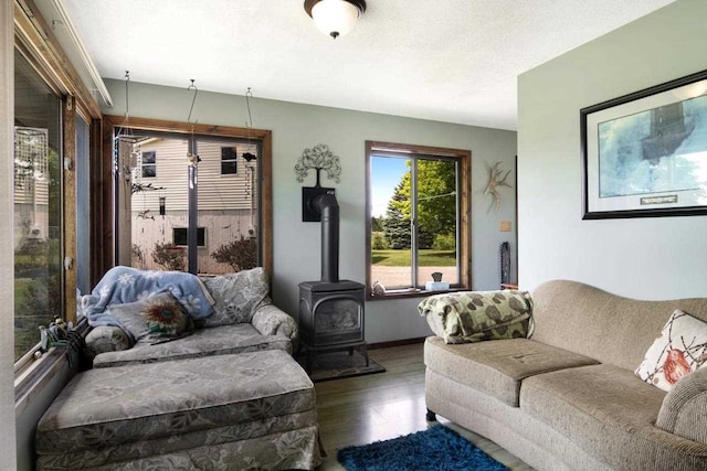 living room featuring a wood stove, wood finished floors, baseboards, and a textured ceiling