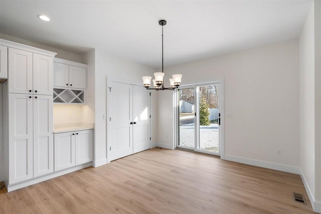 unfurnished dining area featuring visible vents, baseboards, a notable chandelier, and light wood-style flooring