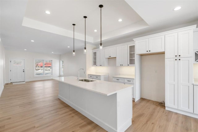 kitchen with a sink, white cabinetry, light wood finished floors, glass insert cabinets, and a raised ceiling