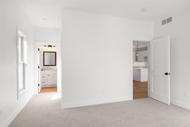 unfurnished bedroom with visible vents, baseboards, light colored carpet, and connected bathroom