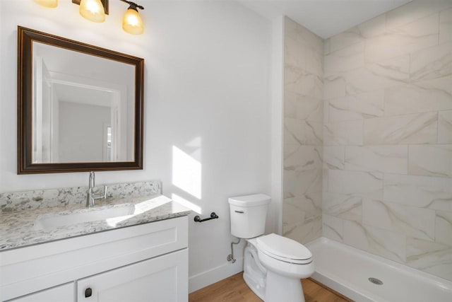 bathroom featuring toilet, wood finished floors, baseboards, tiled shower, and vanity