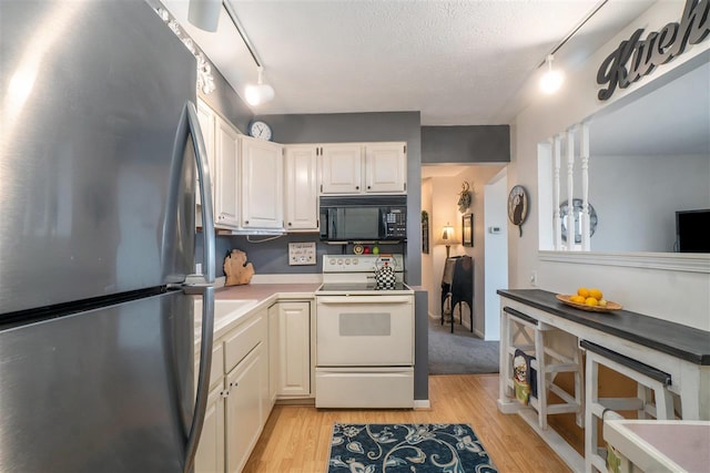 kitchen featuring light wood finished floors, black microwave, electric stove, freestanding refrigerator, and white cabinets