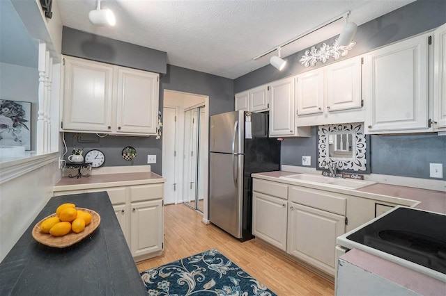 kitchen with white cabinets, electric stove, freestanding refrigerator, and a sink