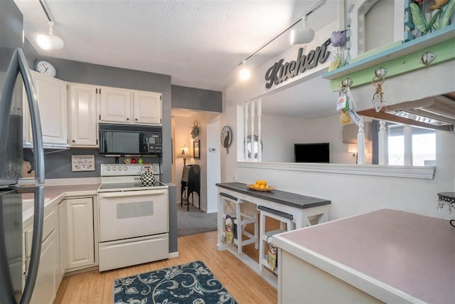 kitchen featuring electric range, light wood-style flooring, freestanding refrigerator, and black microwave