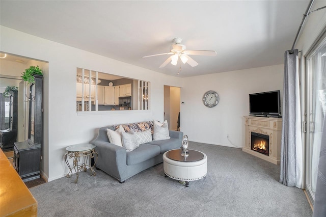 living area featuring baseboards, carpet, a lit fireplace, and a ceiling fan