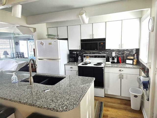 kitchen featuring range with electric cooktop, a sink, backsplash, freestanding refrigerator, and black microwave