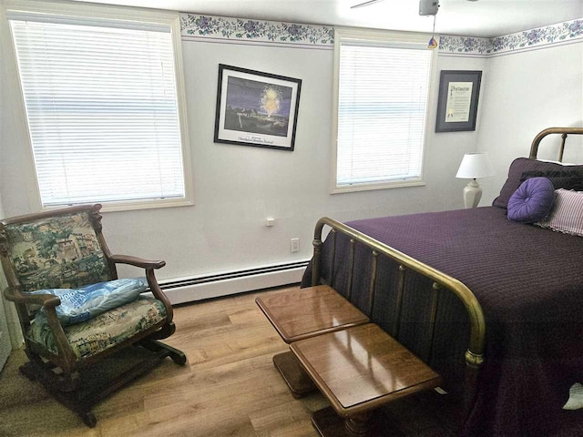 bedroom with a baseboard heating unit, ceiling fan, and wood finished floors