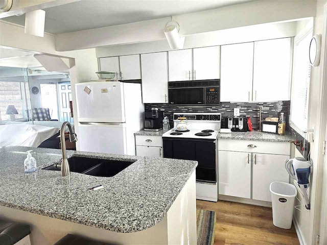 kitchen with tasteful backsplash, black microwave, electric range oven, freestanding refrigerator, and a sink